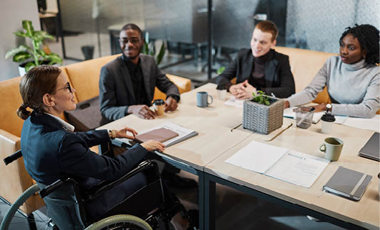 High angle portrait of successful businesswoman using wheelchair at meeting and talking to colleagues in modern office space